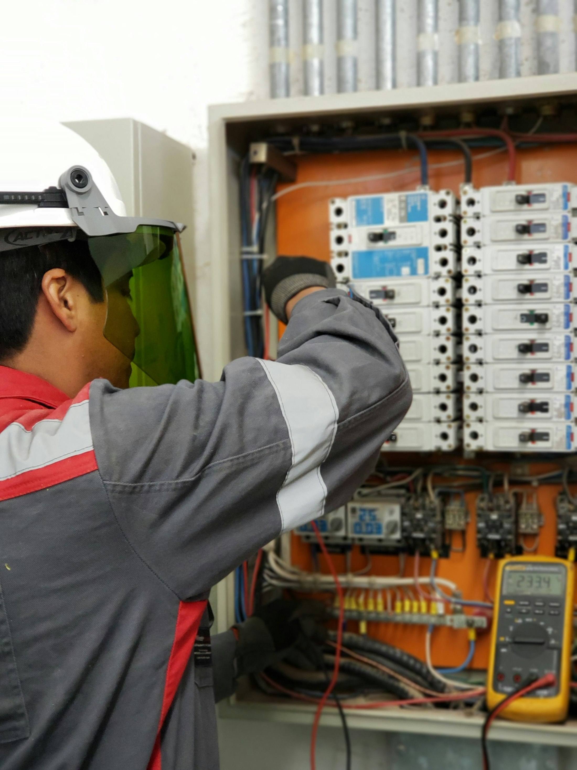 Technician in protective gear testing an electrical control panel